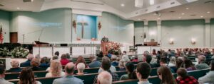 A large congregation listens to a speaker in a modern church setting.